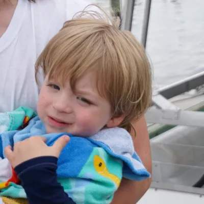 Child wrapped in colorful towel, held by an adult on a boat.