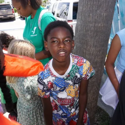 Children gathered outdoors, one boy in a colorful shirt looks at the camera.