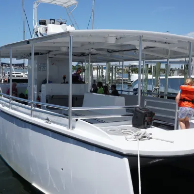 People board a large white tour boat at a dock on a sunny day.