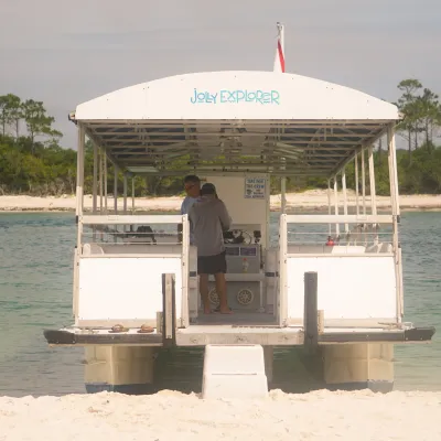 Small white tour boat on sandy shore with trees in background.